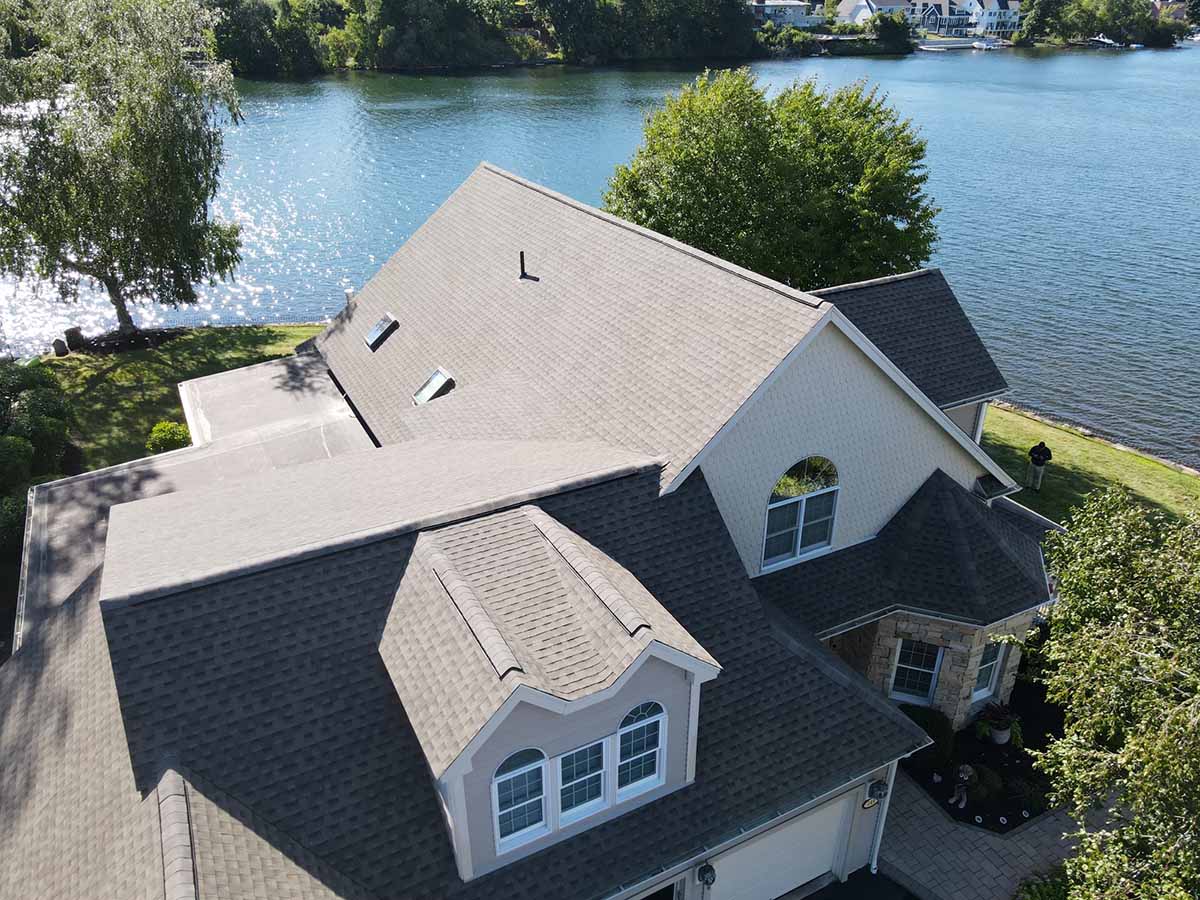 An aerial view of CertainTeed Roofing Shingles on a house with a body of water in the background. CertainTeed Roofing Shingles - CertainTeed vs. Atlas Shingles - January 2023 Blog Post (3) Spring Roof Checklist
