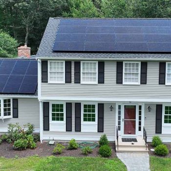 View of a home with newly installed solar panels on two separate roof tops surrounded by large trees