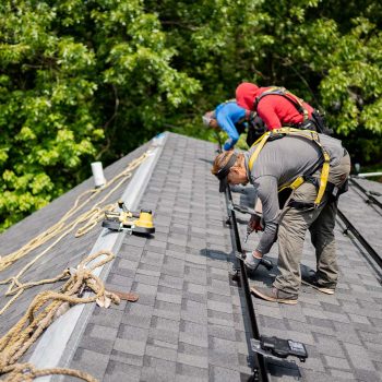 Three Golden Group workers with proper safety equipment installing the foundation for new solar panels on a slanted rooftop.